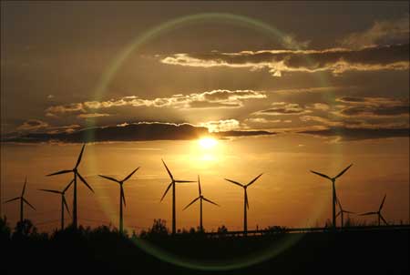 The sun sets behind power-generating windmill turbines.